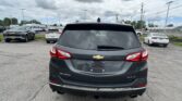 Rear view of a black Chevrolet Equinox SUV in a parking lot, with other cars and a cloudy sky above.