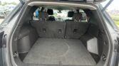 Open SUV hatch reveals spacious cargo area with third-row seats upright and back of car visible in parking lot.