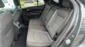Rear passenger seat area of a dark car with quilted fabric seats and visible seat belts, door panel to the left, parked cars outside the window