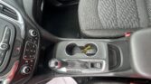 Inside a car showing the center console with gear shifter, cup holder, and control panel next to the textured front seat upholstery.
