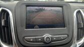 Rearview camera display with orange parking guidelines over a parking lot pavement.