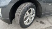 Close-up of a car's front wheel and tire, showing the wheel well and gray SUV fender.