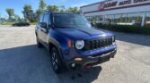 Blue Jeep SUV in the dealership lot with E-Z Loan Auto Sales storefront and large windows in the background, under a bright blue sky.