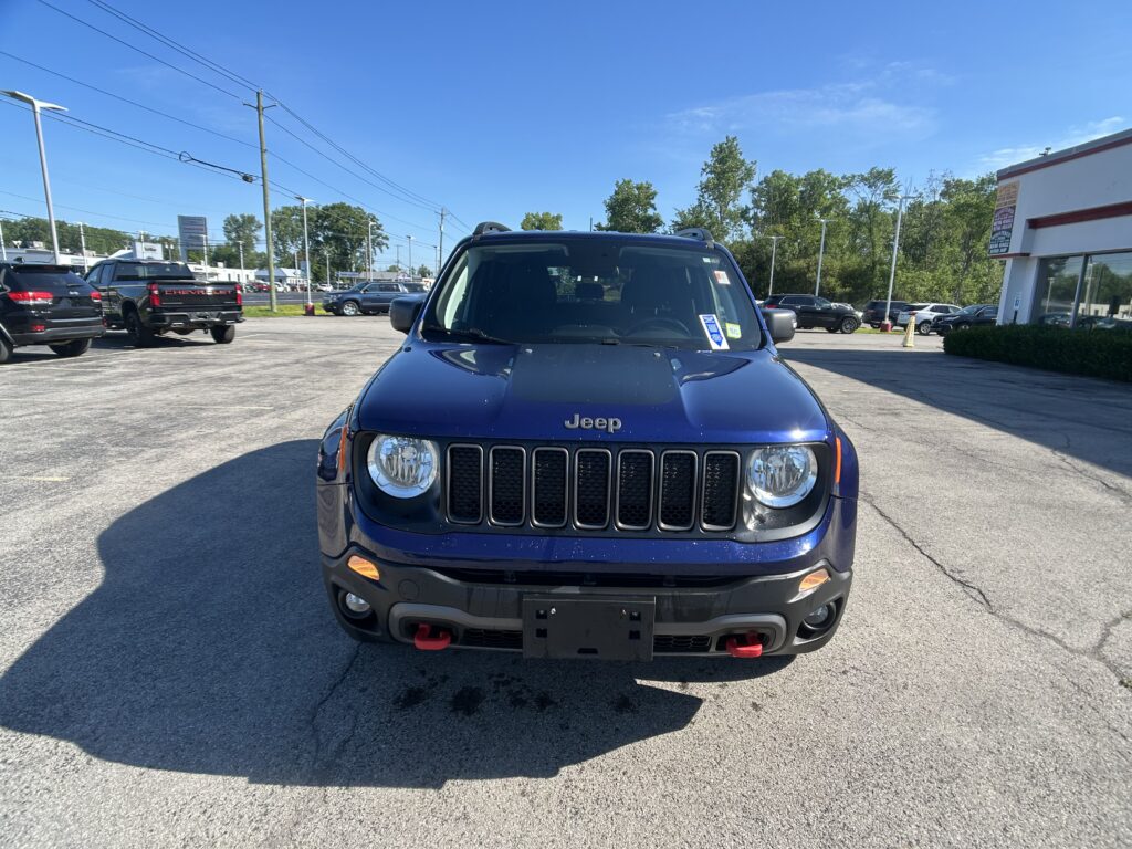 Front view of a blue Jeep in a car dealership lot on a sunny day.