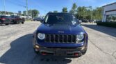 Front view of a blue Jeep in a car dealership lot on a sunny day.