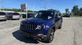Blue Jeep SUV in a dealership parking lot with an EZ Loan Auto Sales sign in the background and other cars nearby.