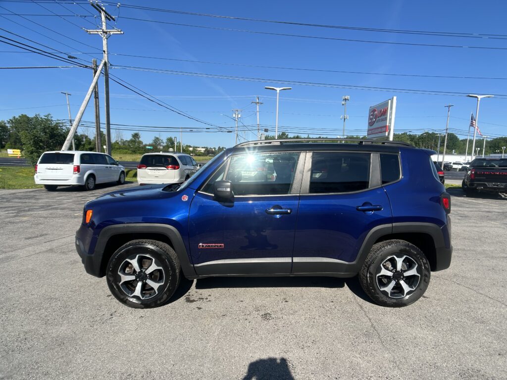 Blue SUV parked in a car dealership lot with other vehicles, power lines, and a clear blue sky in the background.