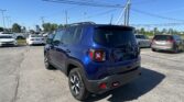 Blue Jeep SUV in a dealership parking lot under a clear blue sky; power lines overhead.
