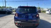 Rear view of a blue Jeep SUV in a parking lot with other cars and overhead power lines under a clear blue sky.