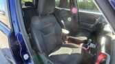Interior of a blue car showing two front seats with 'Trailhawk' embroidery and red stitching, open door, bright sunlight lens flares in window.
