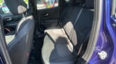 Rear passenger area of a blue car with black fabric seats, headrests, and a view of parked cars through the window on a sunny day.