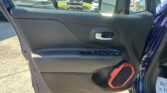 Interior of a car door panel with a chrome handle, window controls, and a red-accented speaker; outside is a parking lot with many vehicles.