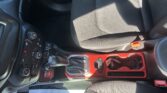 Interior of a car showing the center console with gear shifter and control buttons, red accents on the door and trim, and black fabric seats.