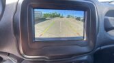 Car's infotainment screen shows the rearview camera view of a parking lot with green/yellow/red guide lines indicating safe distance