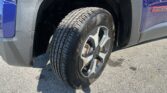 Close-up of a blue pickup truck wheel and tire in the wheel well, showing the rim and tire treads with a dusty fender nearby.