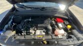 Front view of a car with the hood raised, exposing the engine bay and battery on the passenger side under bright sunlight.
