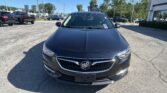 Front view of a dark gray Buick SUV in a dealership lot, with other cars and a building in the background.