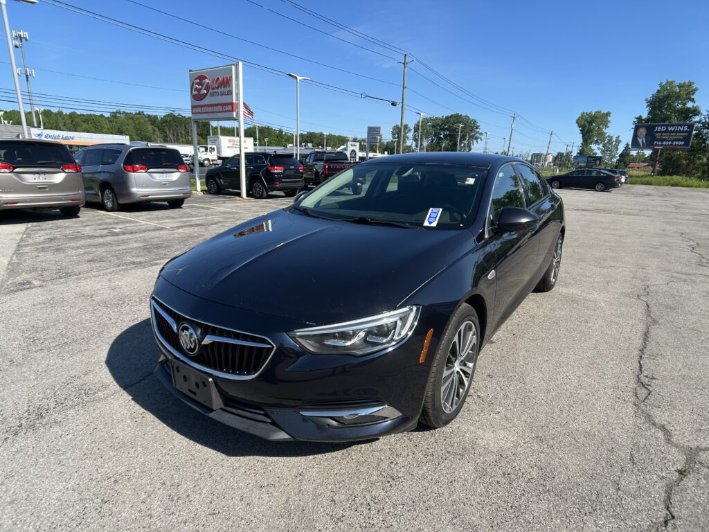 Front-right view of a black Buick sedan in a car dealership lot with other vehicles and an EZ Loan Auto Sales sign in the background on a clear day.