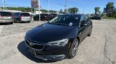 Front-right view of a black Buick sedan in a car dealership lot with other vehicles and an EZ Loan Auto Sales sign in the background on a clear day.