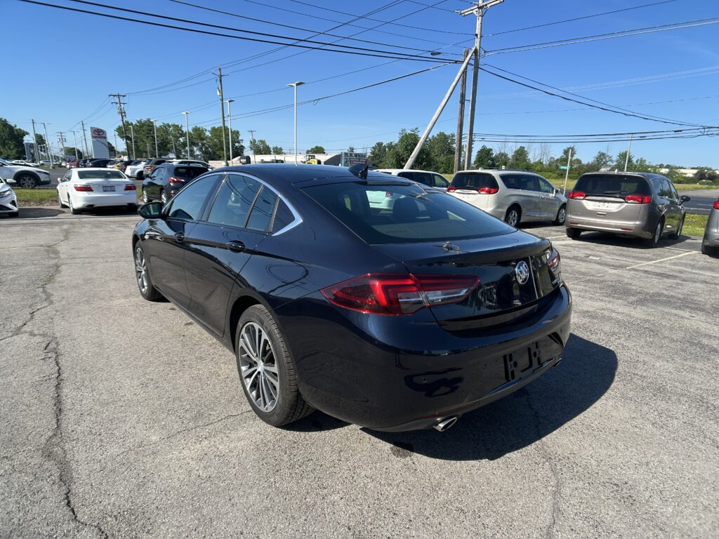 Black sedan in the foreground of a busy parking lot on a sunny day with a clear blue sky and power lines overhead.