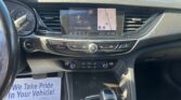 Car dashboard interior showing a central touchscreen with navigation map and radio (96.9 FM), climate controls below, and a gear shifter in foreground.