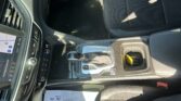 Interior view of a car focusing on the center console: gear shifter, ambient controls, and a touchscreen display showing a map to the left, with cloth seats and a passenger-side floor mat visible.