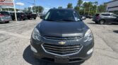 Front view of a gray Chevrolet SUV in a car dealership lot with other vehicles and a large EZ LOAN sign on the left under a clear blue sky.