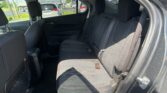 Rear passenger seats in a black fabric car interior with red stitching and three-seat belt arrangement; road traffic visible through the windows.