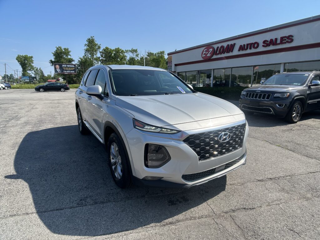 Front corner of a white Hyundai SUV in a dealership lot with EZ LOAN AUTO SALES building in background.