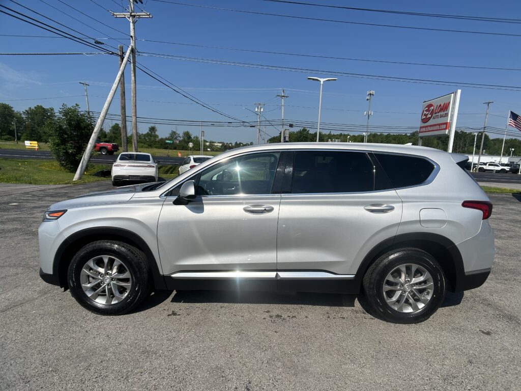 Side view of a silver SUV parked in a car lot with power lines and a sign in the background.
