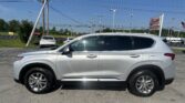 Side view of a silver SUV parked in a car lot with power lines and a sign in the background.