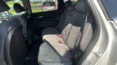 Rear passenger seats in a dark fabric SUV, showing three seat belts and headrests, with a gray SUV visible through the window outside.