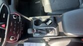 Center console area of a car interior with gear shifter, cup holders, and climate controls; a paper lies on the floor near the passenger seat.