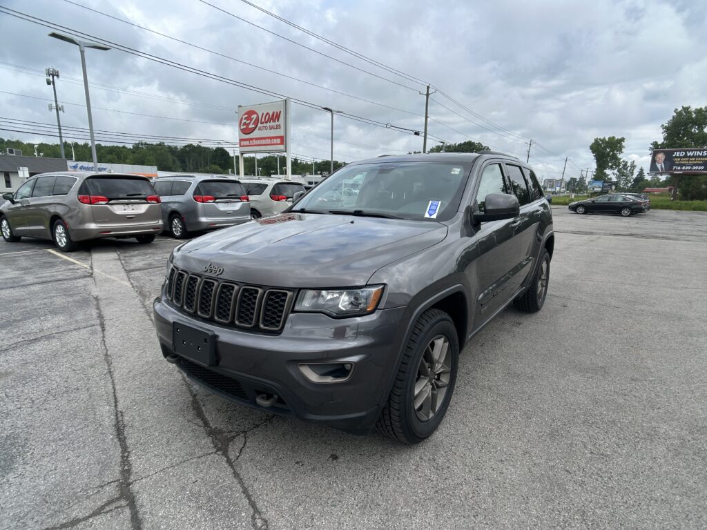 Gray Jeep SUV in the foreground at a car dealership lot, with an EZ Auto Sales sign and cloudy sky in the background.