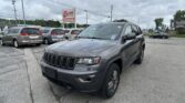 Gray Jeep SUV in the foreground at a car dealership lot, with an EZ Auto Sales sign and cloudy sky in the background.