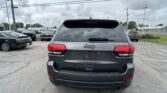 Rear view of a gray Jeep SUV in a parking lot under cloudy skies with other cars around it.