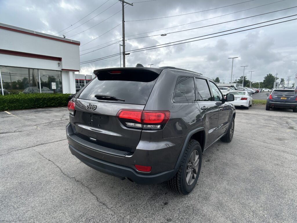 Gray Jeep SUV shown from rear-right in a dealership lot, with a white building and cloudy sky in the background.