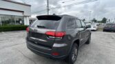 Gray Jeep SUV shown from rear-right in a dealership lot, with a white building and cloudy sky in the background.