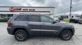 Gray Jeep Grand Cherokee SUV parked in the lot in front of E-Z Loan Auto Sales storefronts under a cloudy sky.