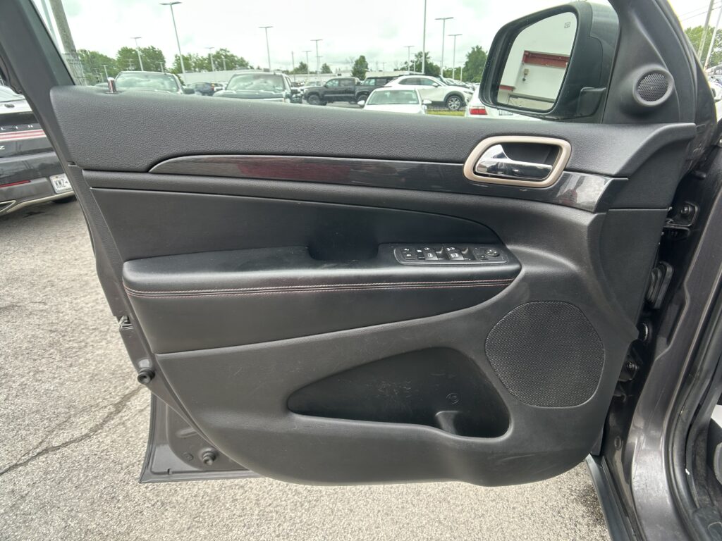 Inside of a car door panel showing window controls near the armrest and a chrome door handle, with a view of a parking lot outside the window.