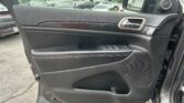 Inside of a car door panel showing window controls near the armrest and a chrome door handle, with a view of a parking lot outside the window.