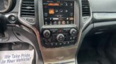 Center console of a car with a touchscreen climate control panel, dials, and cup holder visible; paper flyer on the floor reads 'We Take Pride In Your Vehicle!'