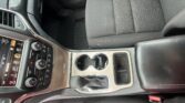 Front passenger area of a modern car, showing center console, cup holders, gear shifter, and black seats with red stitching.