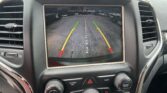 Rearview camera display on car console showing parking guidelines with green, yellow, and red lines in a lot. Text reads 'Check Entire Surroundings'.
