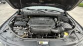 Open-hood view of a vehicle's engine compartment, dominated by a V6 engine cover and surrounding components (battery, hoses, and wiring).