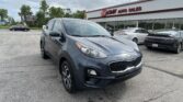 Gray Kia SUV parked in foreground outside EZ Loan Auto Sales dealership with other cars and a billboard in the background.