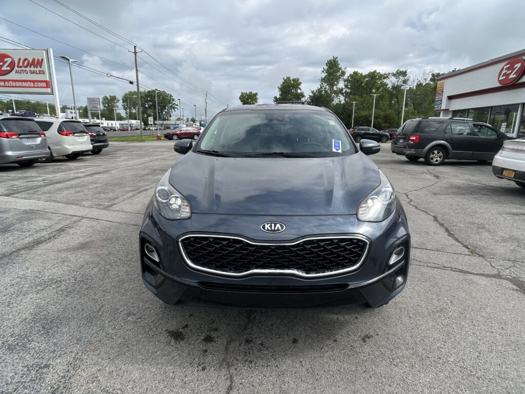 Front view of a gray Kia SUV parked in a used-car lot, EZ Auto Sales building visible on the right.