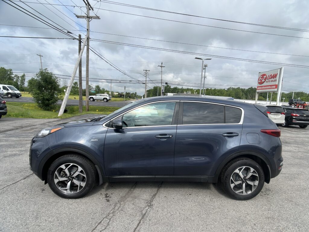 Front-side view of a gray Kia SUV in a parking lot, with a dealership sign and power lines in the background.