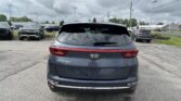 Rear view of a gray Kia Sportage in a parking lot with other cars and a cloudy sky above.