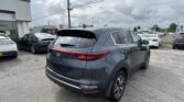 Gray Kia SUV in the foreground of a dealership lot with multiple cars and a Toyota showroom in the distance.